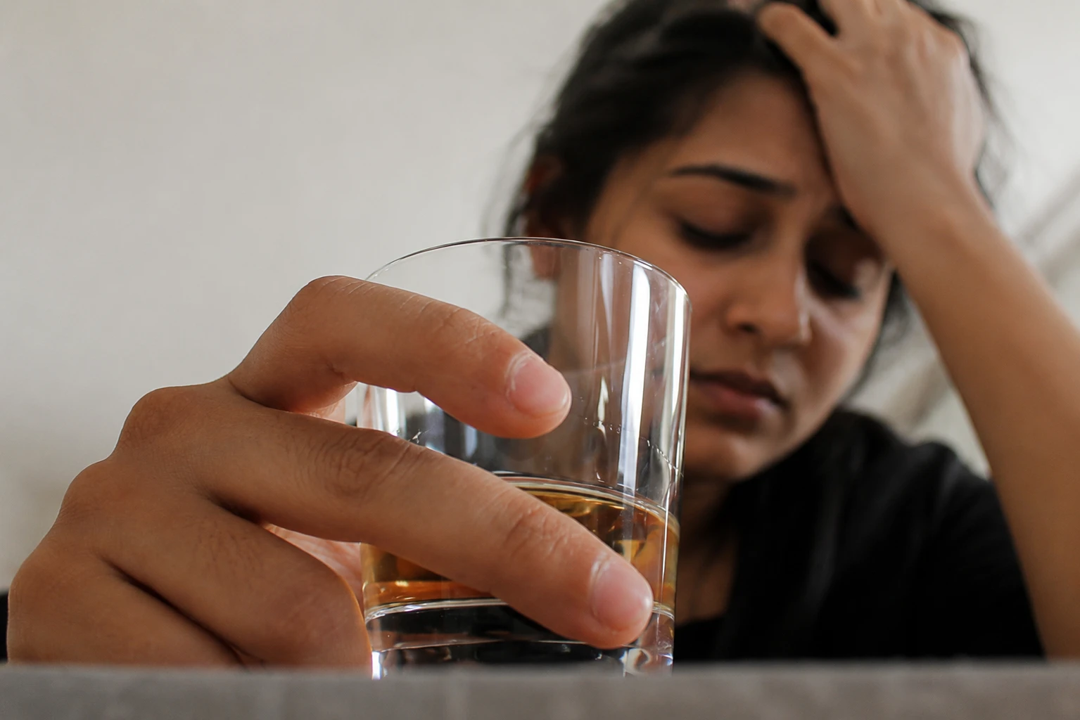 A woman sitting alone at home with a glass of alcohol, illustrating hidden drinking